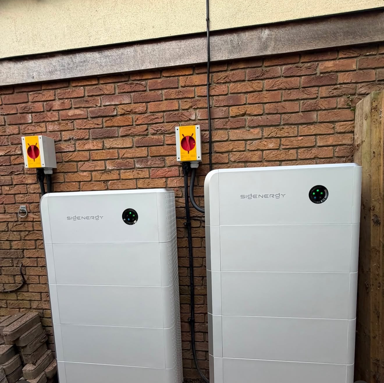 Two tall stacked battery towers installed outdoors against a brick wall