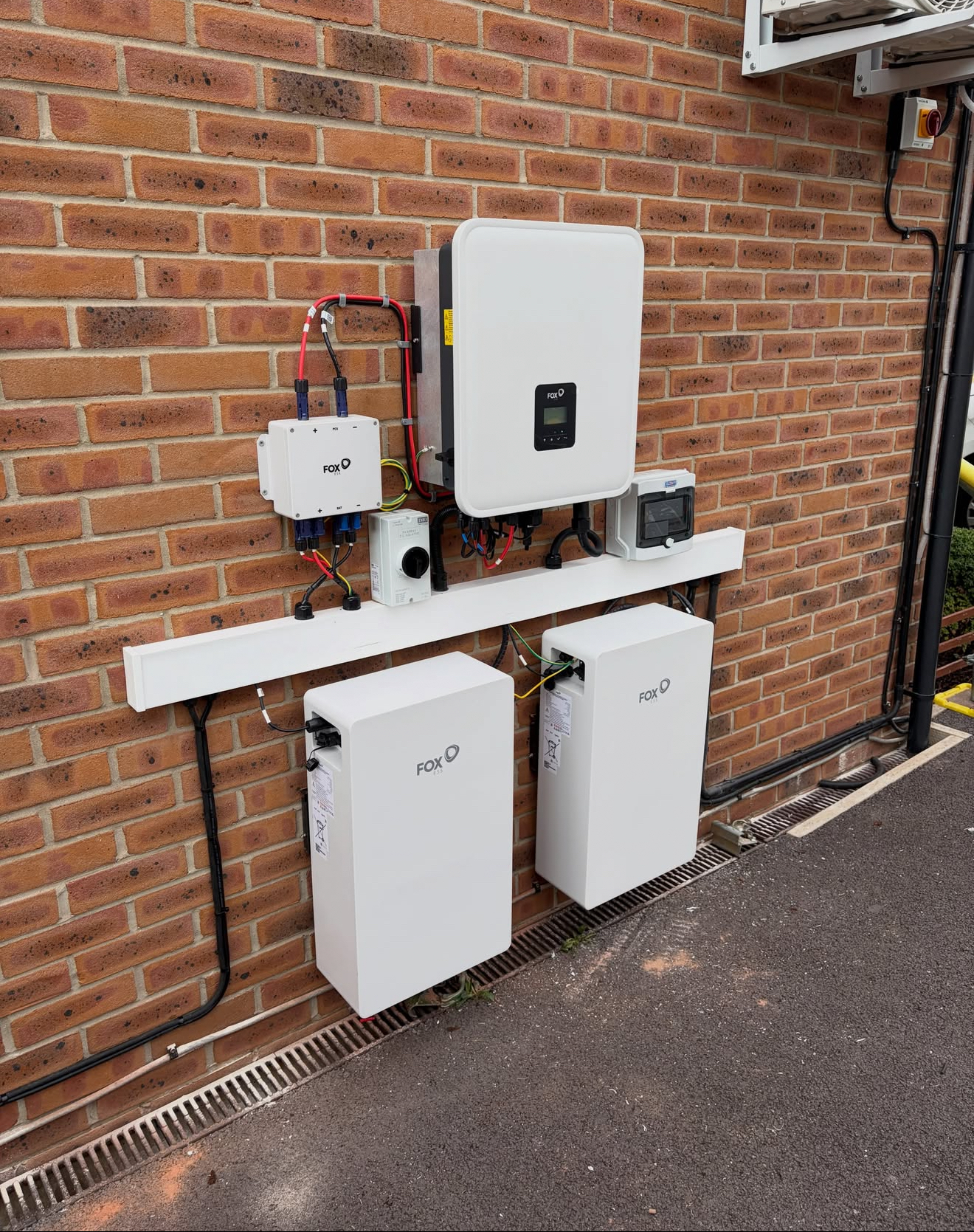 Hybrid inverter and two battery modules mounted on a red brick wall outdoors