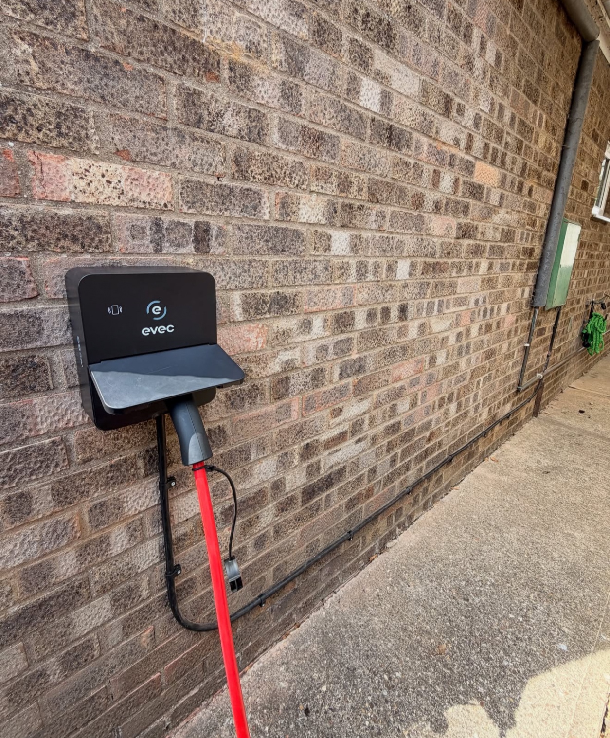 evec EV charger with cable holder on a dark brick wall