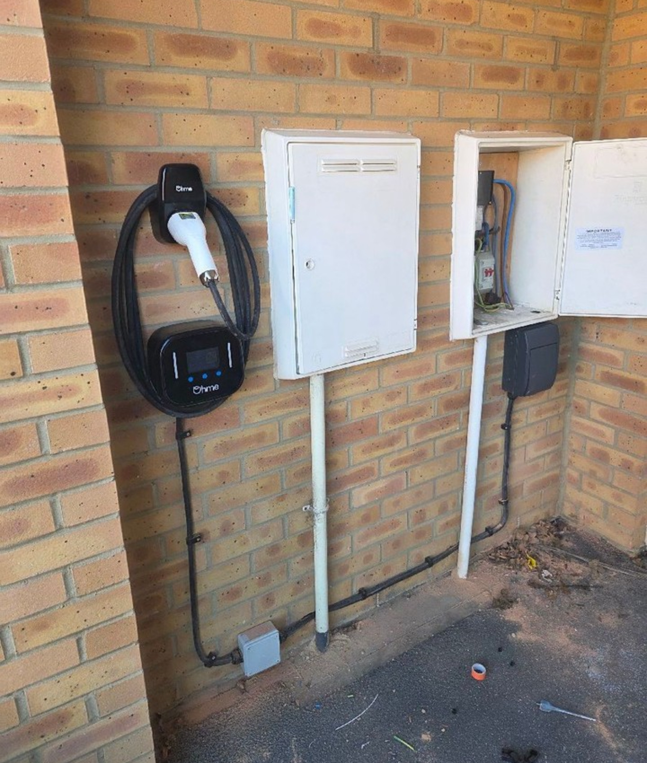 Ohme EV charger installed alongside consumer unit boxes on a brick wall