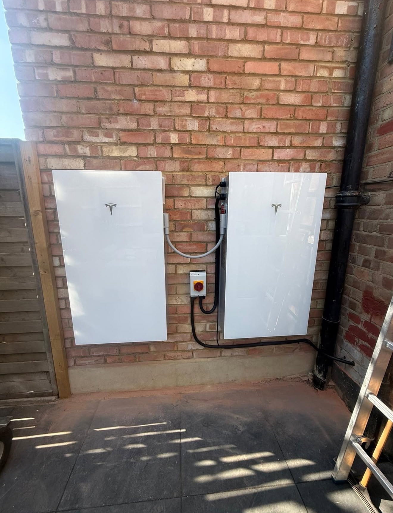 Two white home batteries mounted side by side on a red brick wall